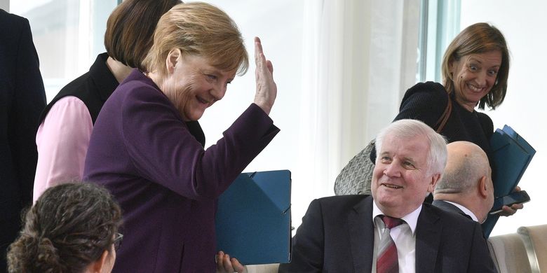 Kanselir Jerman Angela Merkel (kiri) tertawa seraya mengangkat tangannya pada 2 Maret 2020. Momen itu terjadi setelah Menteri Dalam Negeri Horst Seehofer menolak jabat tangan dengannya di tengah penyebaran virus corona.