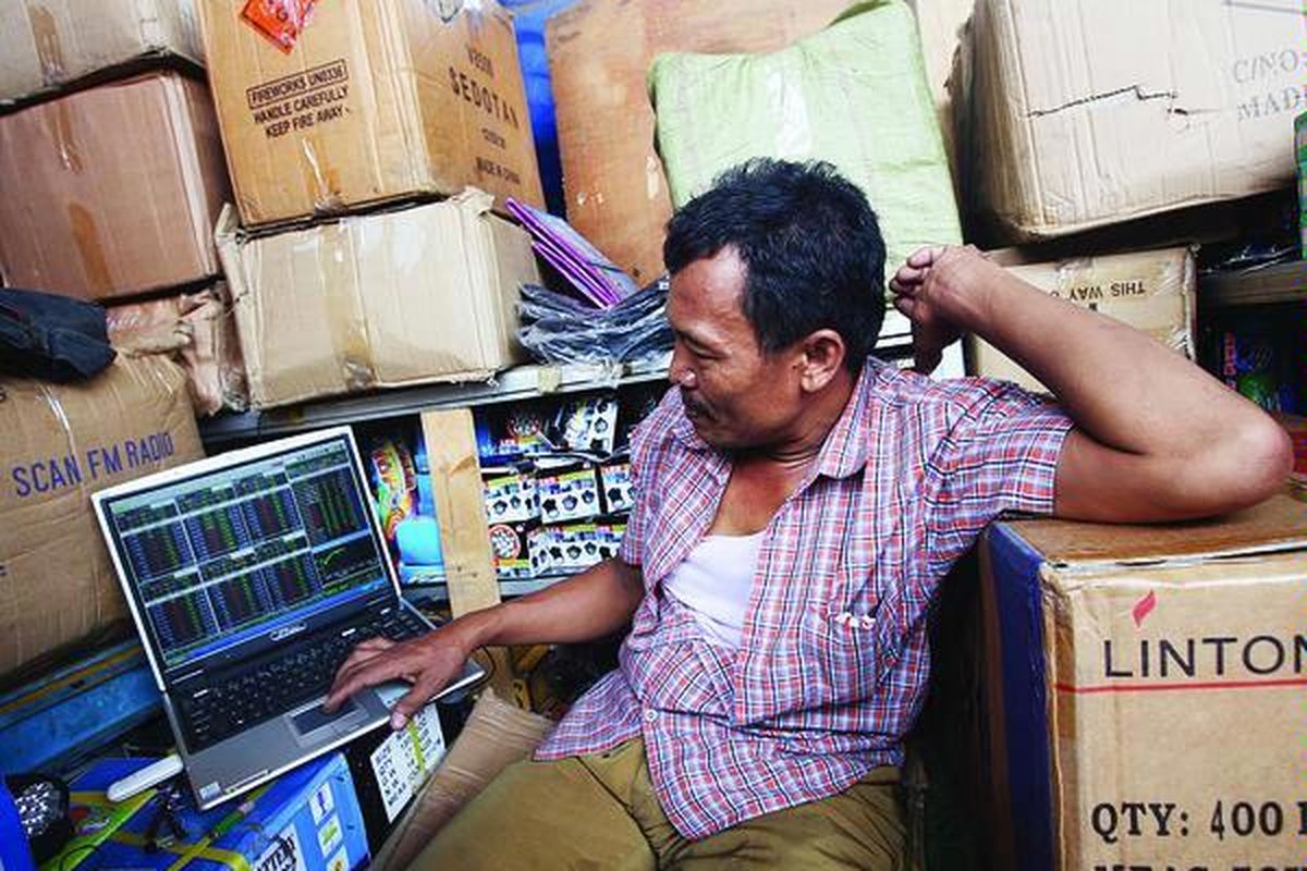Supriyanto, pedagang grosiran di bawah jembatan layang Asemka, Jakarta Barat, memantau harga saham miliknya dengan laptop yang terkoneksi dengan internet, Rabu (3/2). Dia sudah dua tahun berinvestasi di pasar modal walaupun pernah merugi puluhan juta rupiah.