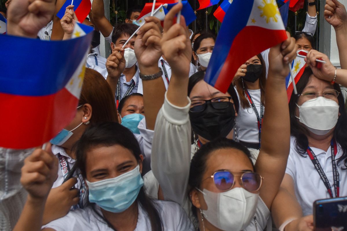 Government employees wave their national flags as they await the arrival of their new Philippine President Ferdinand Marcos Jr. at the Malacanang presidential palace, following his inauguration ceremony in Manila on June 30, 2022. (Photo by Maria Tan / AFP)