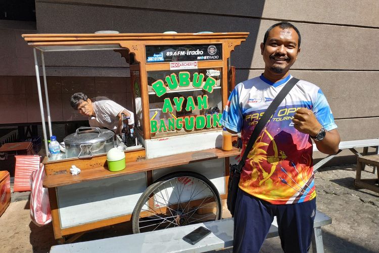 Kholidin alias Bang Udin (42), difabel yang berprofesi sebagai tukang bubur mengenakan jersey panahan berpose di depan gerobaknya di parkiran mobil Wisma Geha, Jakarta Pusat, Selasa (10/9/2019).