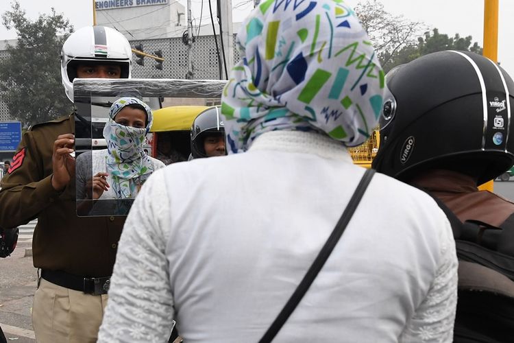 Polisi lalu lintas di Delhi, Sandeep Shahi (kiri) mengangkat cermin dan mengarahkannya ke seorang pembonceng yang tidak mengenakan helm.