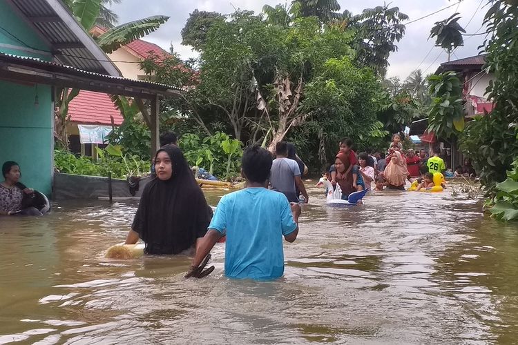 Sejumlah warga di Desa Pulau Rambai, Kecamatan Kampa, Kabupaten Kampar, Riau, mengarungi genangan banjir, Minggu (15/12/2019) sore. Sebagian dari mereka baru saja dari luar membeli makanan dan kembali lagi ke rumahnya.