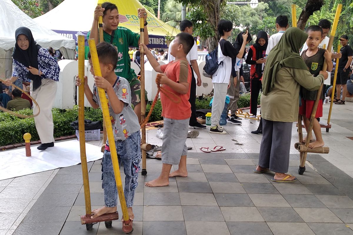 Anak-anak pengunjung Car Free Day (CFD) Taman Bungkul, Surabaya saat mencoba permainan egrang di stan Kampoeng Dolanan, Minggu (23/2/2025).