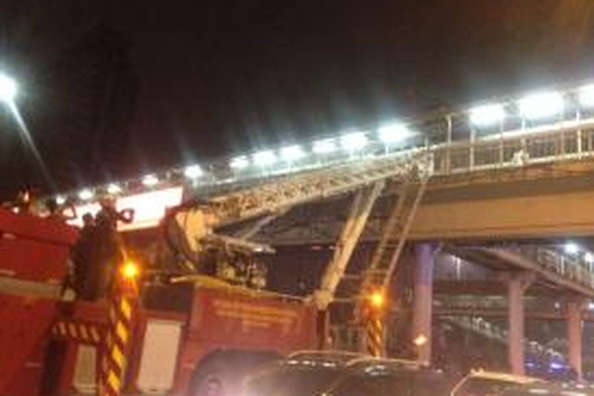 Seorang laki-laki yang ditakutkan akan bunuh diri berdiri di atas atap jembatan penyeberangan orang di depan Plaza Semanggi, Sabtu (4/4/2015) dini hari sementara mobil pemadam kebakaran yg dilengkapi tangga bersiap di bawahnya.