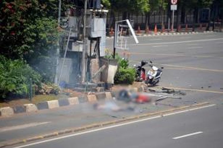 Dua jenazah terlihat di tepi jalan sebelah pos polisi yang rusak setelah ledakan menghantam kawasan Jalan MH Thamrin, Jakarta Pusat, 14 Januari 2016. Serangkaian ledakan menewaskan sejumlah orang, terjadi baku tembak antara polisi dan beberapa orang yang diduga pelaku.