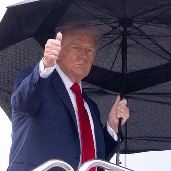 Presiden Amerika Serikat Donald Trump mengacungkan jempol sambil membawa payung saat akan menaiki pesawat kepresidenan Air Force One untuk berangkat ke Israel, dari Pangkalan Udara Gabungan Saint Andrews di Maryland, Minggu (12/10/2025).