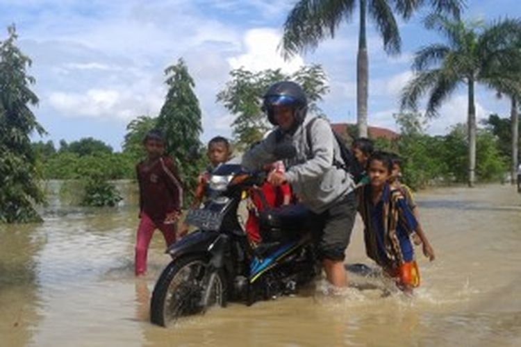 Pengendara roda dua melintas di Jalan Desa Jalmak, tepatnya di depan kantor Dinas Pertanian. Di lokasi tersebut ketinggian air mencapai 1,5 meter. 