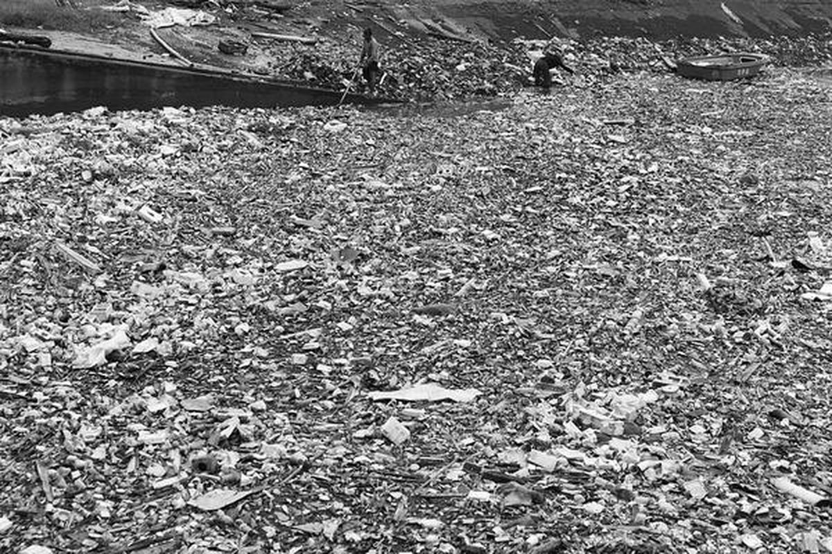 Pekerja mengumpulkan sampah yang memenuhi pintu air Kanal Timur di Ujung Menteng, Cakung, Jakarta Timur, Selasa (27/12). Sampah dan sedimentasi lumpur membuat pendangkalan kanal berlangsung cepat.