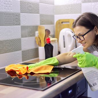 Ilustrasi wanita sedang membersihkan kompor kaca. 