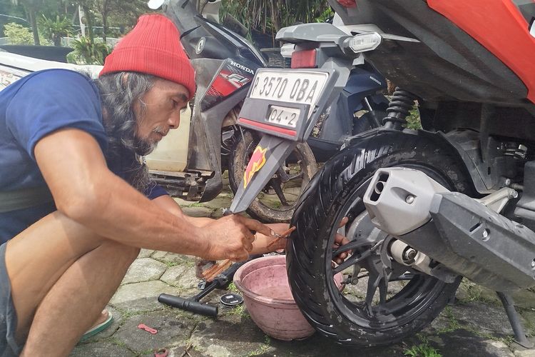 Budyono bekerja sebagai tukang tambal ban. Ia tengah menambal ban pada Jumat (24/1/2025). Budy siap melayani panggilan selama 24 jam di Kecamatan Banyuwangi.