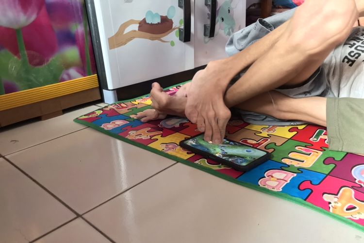Azriel Ilhami Pasha (16) sedang bermain game Mobile Legend dengan kakinya sambil berbaring di rumahnya di kawasan Tanjung Barat, Jagakarsa, Jakarta Selatan pada Rabu (14/6/2023) siang. Azriel mengalami kerusakan jaringan otak sejak lahir alias Celebral Palsy sehingga terbatas dalam bergerak.