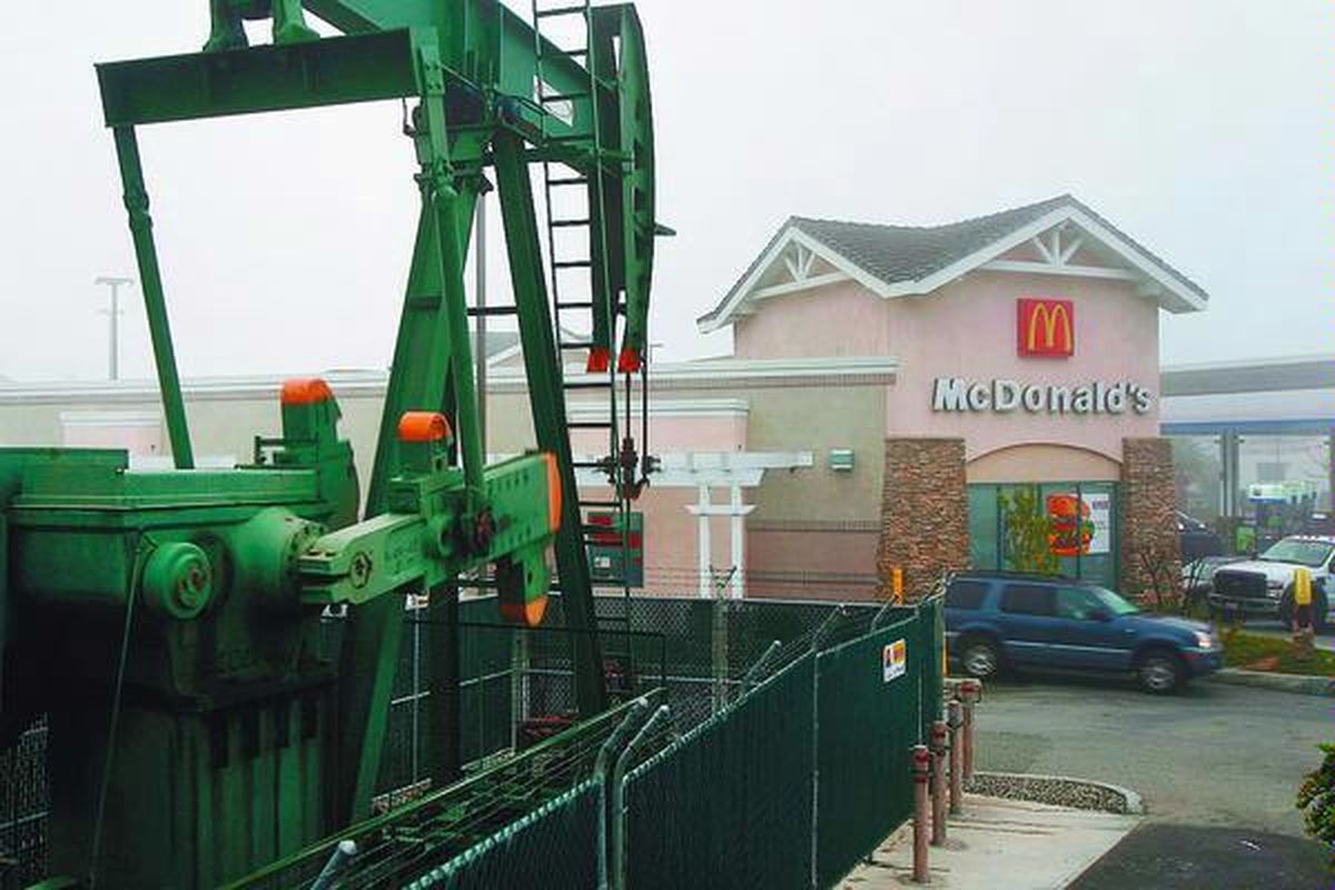 Sebuah pompa ladang minyak mentah tampak di dekat sebuah restoran siap saji di Signal Hill, California, Amerika Serikat, 6 Maret. Harga minyak dunia yang sempat melewati 106 dollar AS per barrel membuat produksi minyak bergiat.  