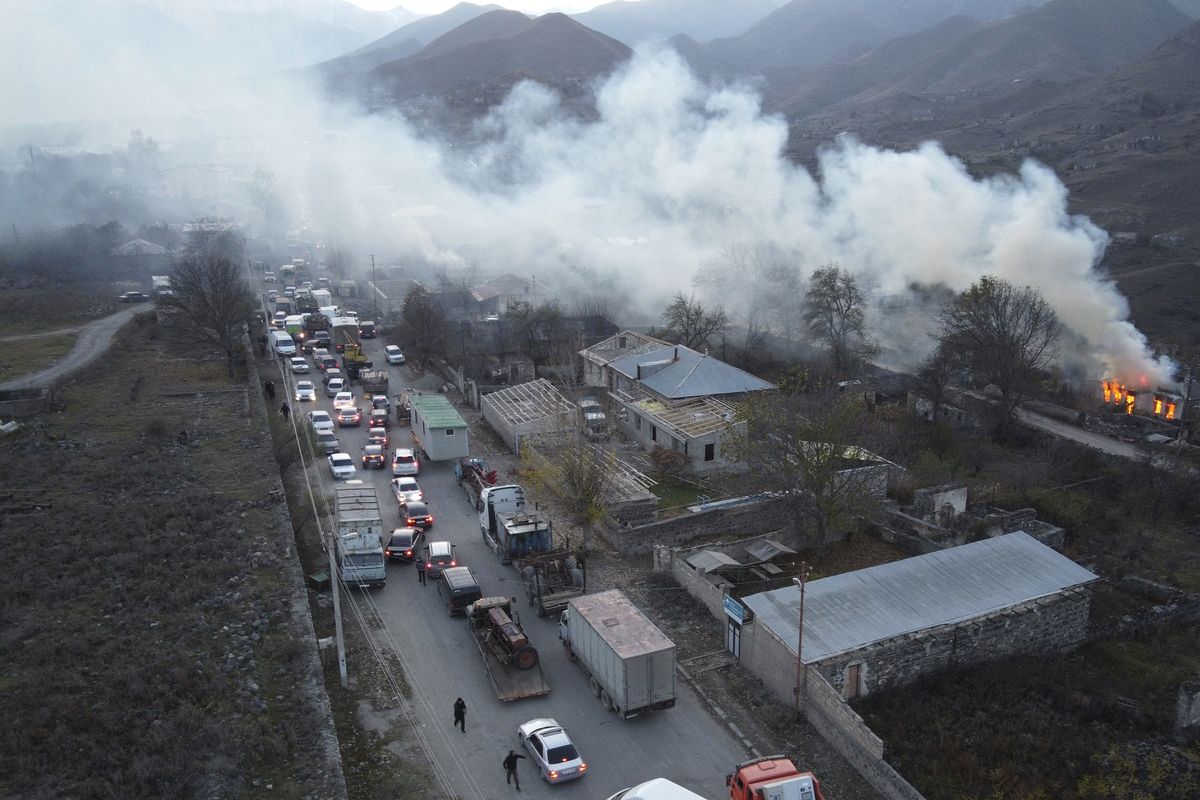 Asap mengepul dari rumah yang terbakar di Nagorno-Karabakh, dan kendaraan terjebak macet di jalan Kaljabar yang menuju Armenia pada Sabtu (14/11/2020). Wilayah itu akan diserahkan ke Azerbaijan sesuai kesepakatan damai untuk mengakhiri perang selama 6 minggu. Setelah dua tahun, hubungan Armenia dan Azerbaijan kini kembali memanas.