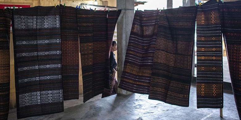 Warga melintas di antara tenun ikat di Pasar Alok, Maumere, Sikka, Nusa Tenggara Timur (NTT), Selasa (31/7/2018). Di Pasar Alok, setiap Selasa mulai pukul 06.0013.00 Wita merupakan hari khusus bagi perajin seantero Kabupaten Sikka dan daerah lainnya untuk menjual kain tenun ikat hasil kerajinan tangan yang dibuat dengan mesin tenun tradisonal.