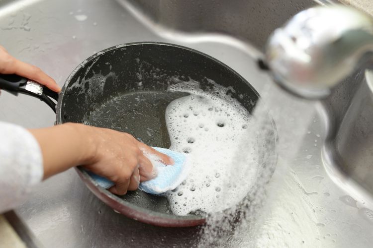 Ilustrasi seseorang sedang mencuci teflon dengan sabun dan air mengalir. 