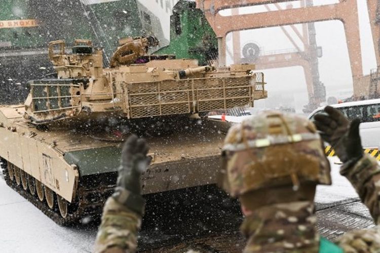 Seorang prajurit Angkatan Darat AS memberi isyarat jalan ke tank tempur M1A2 Abrams yang akan digunakan untuk latihan militer oleh Tim Tempur Brigade Lapis Baja ke-2, di Terminal Kontainer Baltik di Gdynia pada 3 Desember 2022. Peralatan militer tiba di Polandia sebagai bagian dari Operasi Atlantic Resolve, menambah kehadiran udara, darat dan laut di sepanjang sisi timur NATO. 