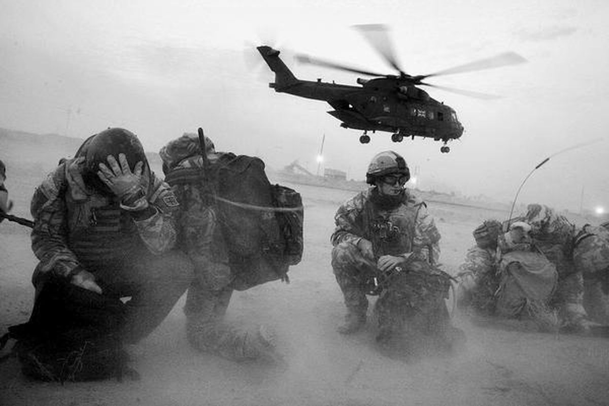 Tentara Inggris dari 51 Squadron berlindung dari debu yang terembus akibat kibasan baling-baling helikopter saat melakukan tugas pengamanan di Basra, Irak selatan, pada 9 Februari 2009. Sebagian warga Inggris menentang invasi ke Irak yang diprakarsai AS.