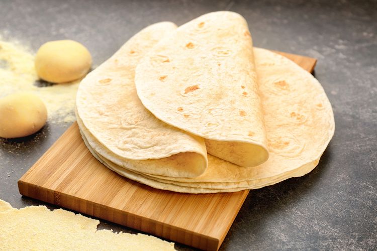 Ilustrasi tumpukan tortila khas Meksiko di atas talenan. 