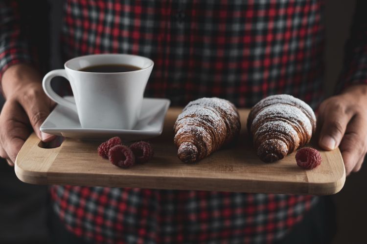 Ilustrasi pelayan membawa kopi dan croissant ala kafe. 