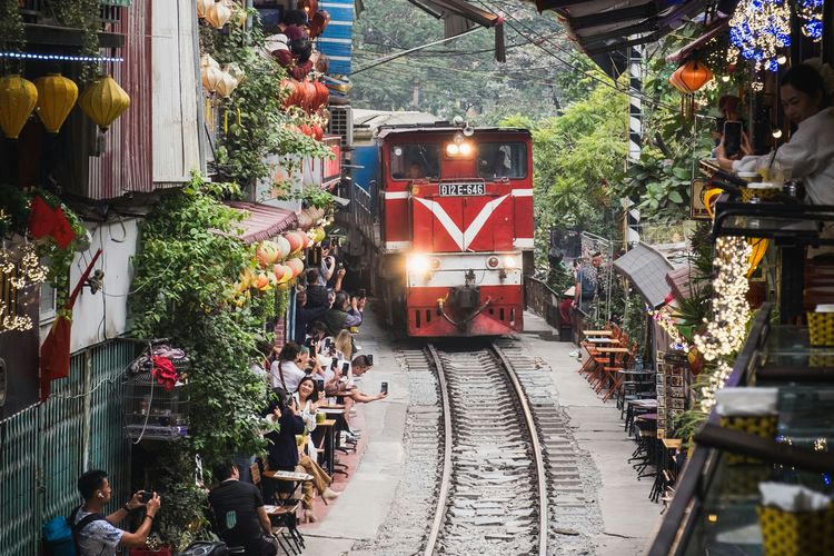 Ilustrasi wisatawan memotret kereta yang lewat di kafe rel kereta api di Vietnam.