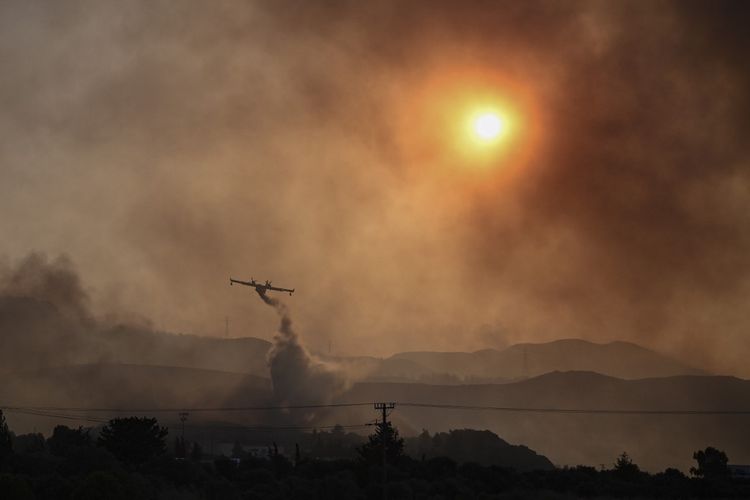 Sebuah pesawat pemadam kebakaran milik maskapai penerbangan Canadair menyemprotkan air ke arah api di Gennadi, di bagian selatan pulau Rhodes, Yunani, pada 25 Juli 2023, saat terjadi kebakaran hutan. Kebakaran hutan Yunani di tengah suhu udara yang sangat panas, memaksa evakuasi massal di beberapa tempat wisata termasuk di pulau Rhodes dan Corfu. 