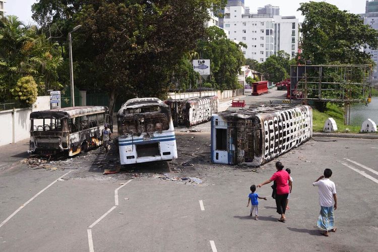 Sebuah keluarga Sri Lanka menyaksikan puing-puing bus yang terbakar dalam bentrokan di Kolombo, Sri Lanka, Rabu, 11 Mei 2022. 