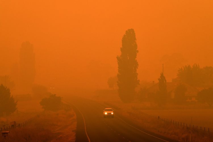 Sebuah mobil melintasi jalanan Bemboka, Negara Bagian New South Wales, Australia, di tengah kabut yang membuat langit seolah menjadi oranye pada 5 Januari 2020. Sebanyak 24 orang dilaporkan tewas sejak kebakaran hutan melanda Australia pada September lalu.