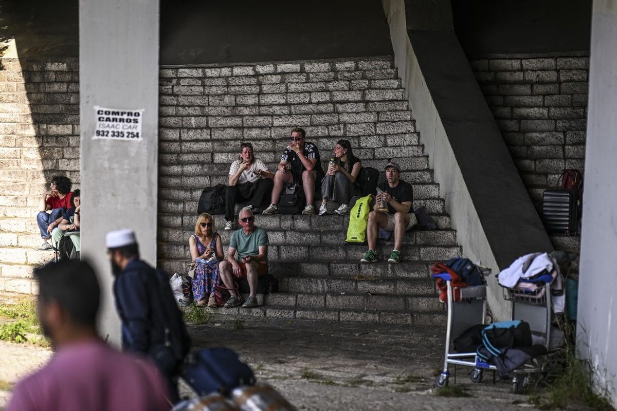 Para pelancong dengan barang bawaan mereka berlindung dari sinar matahari di bawah jembatan setelah meninggalkan Bandara Humberto Delgado di Lisbon, Portugal, sehubungan dengan adanya peristiwa Spanyol-Portugal mati listrik pada Senin (28/4/2025), yang memutus jaringan ponsel dan internet, menghentikan kereta api, dan membuat orang-orang terjebak di dalam lift.