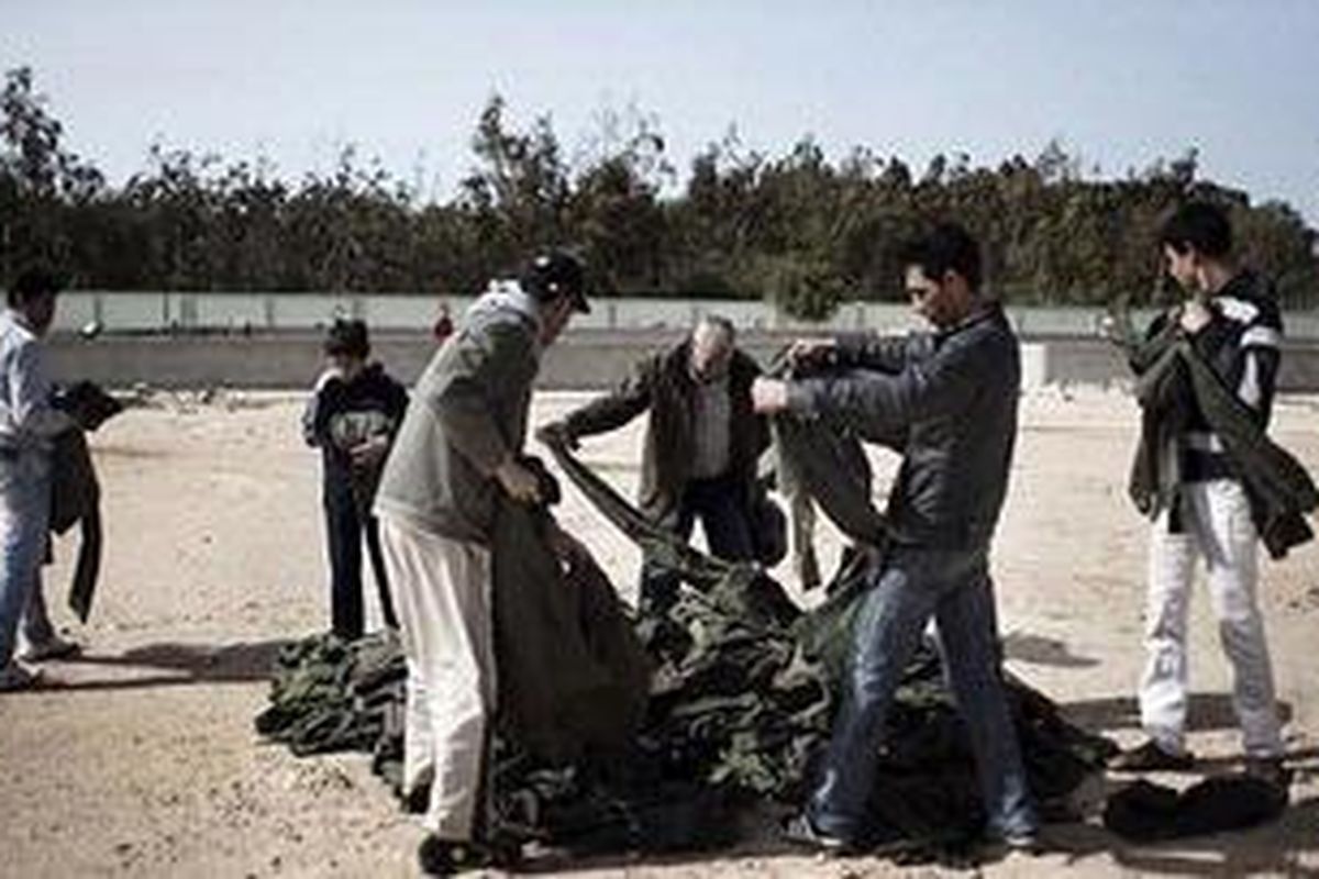 Warga sipil Libya, Selasa (1/3/2011) mencari seragam yang cocok dengan ukuran badan mereka di antara tumpukan pakaian militer setelah mereka terdaftar sebagai anggota milisi yang berjuang di pihak oposisi di Benghazi, Libya Timur.
