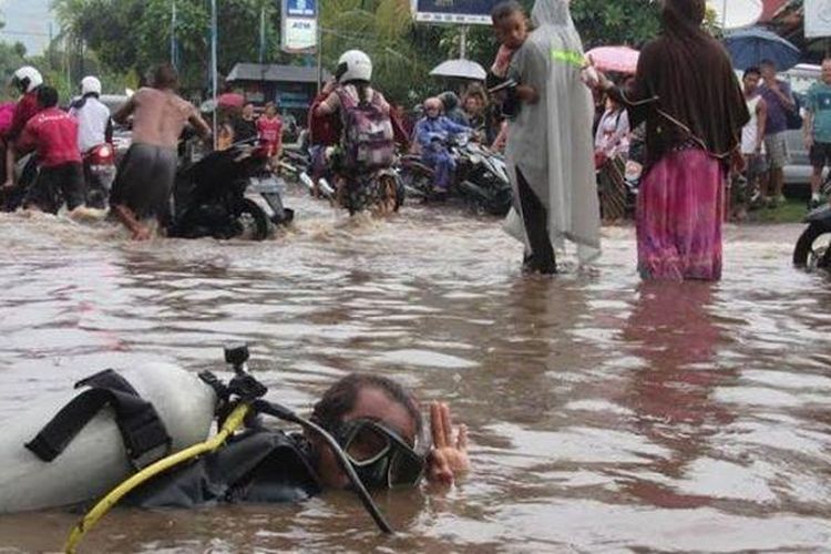 Putu Sudarimbawa saat melakukan aksi diving di tengah Jalan Raya Singaraja-Gilimanuk, Desa Pemuteran, Kecamatan Gerokgak, Buleleng yang tergenang banjir, Rabu (25/1/2017). 