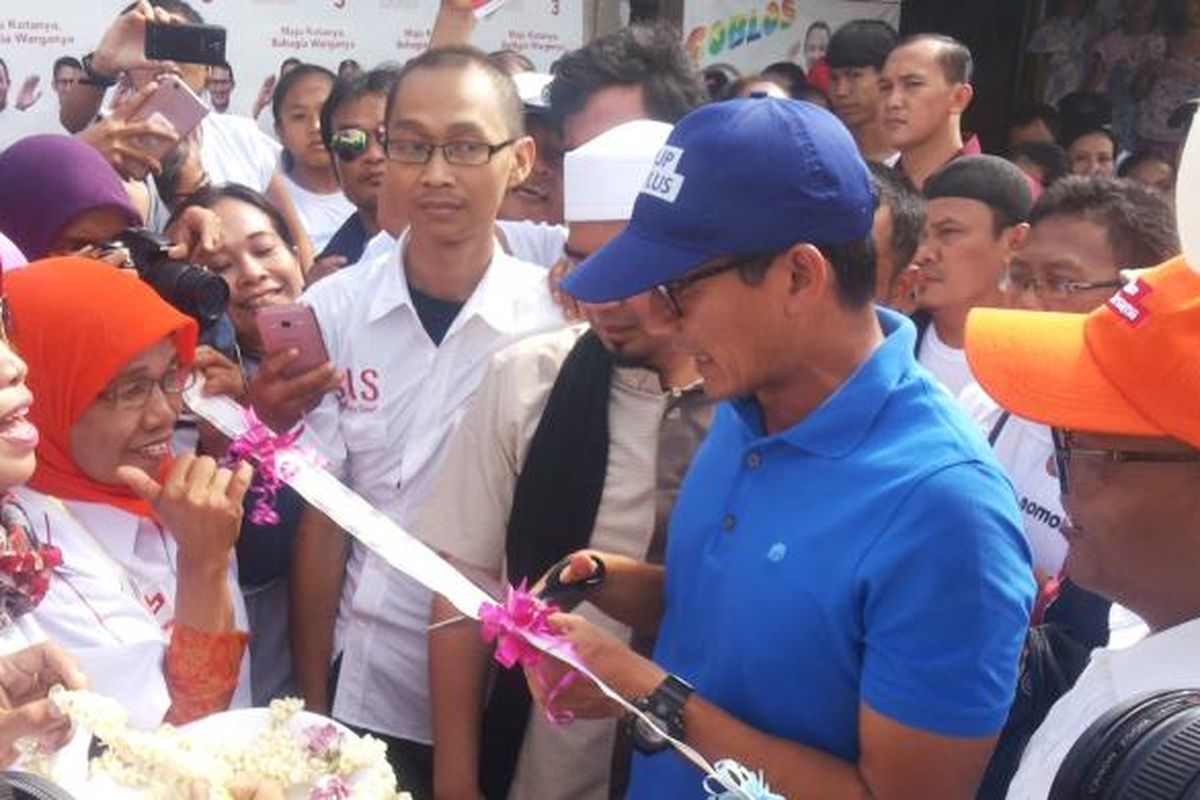 Calon wakil gubernur DKI Jakarta nomor pemilihan tiga Sandiaga Uno menggunting pita yang disiapkan warga saat kedatangannya di Kampung Kebon Bayam, Kelurahan Papanggo, Tanjung Priok, Jakarta Utara, Rabu (25/1/2017). Pita disiapkan warga untuk menandai perubahan nama kampungnya menjadi kampung Anies-Sandi.