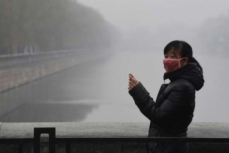 Seorang wanita mengenakan masker wajah saat mengambil foto di sekitar Forbidden City yang diselimuti oleh kabut asap polusi udara, Selasa, 8 Desember 2015. Pemerintah Kota Beijing, Senin sore, untuk pertama kalinya dalam sejarah menaikan status kabut menjadi darurat berstatus ?berwarna merah? yang merupakan status darurat paling tinggi.