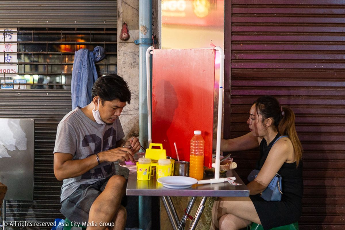 Terlihat dua orang yang sedang makan di meja yang sama di Yaowarat, Bangkok, tapi dibatasi dengan papan di antara mereka untuk menjaga jarak aman dalam masa lockdown di Bangkok, Thailand