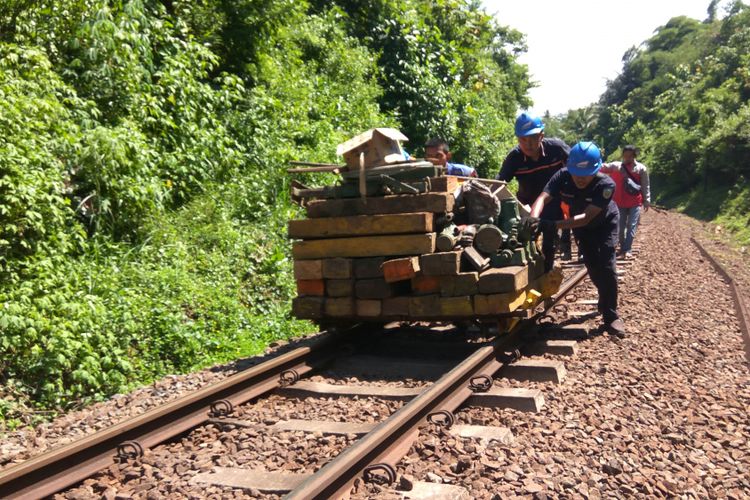 Petugas mendorong lori yang berisi bantalan kayu, dongkrak. Alat evakuasi terpaksa diangkut lori karena tidak ada akses kendaraan ke lokasi anjloknya KA Malabar, Jumat (2/2/2019). 