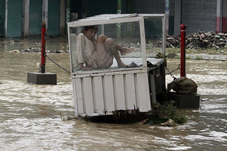 Seorang anak laki-laki berdiam diri di dalam kios yang mengapung di atas banjir Pakistan di Peshawar, Sabtu (27/8/2022). Menurut pemerintah, banjir di Pakistan dipicu hujan muson lebat di seluruh negara, menewaskan hampir 1.000 orang dan membuat ribuan warga mengungsi sejak pertengahan Juni.