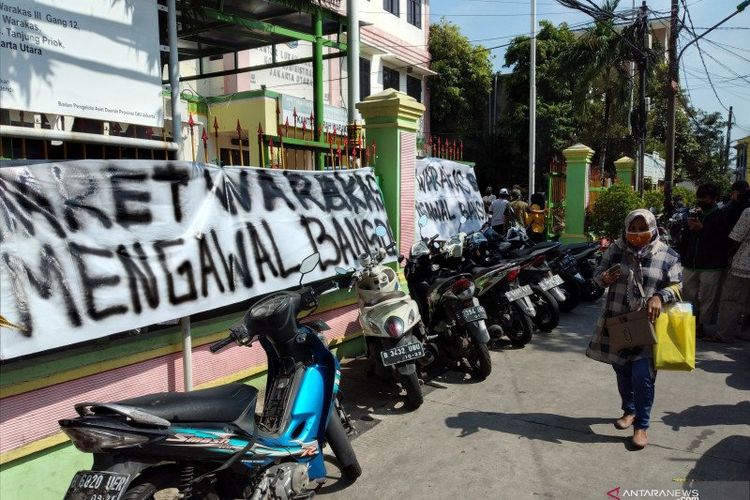 Seorang warga berjalan di depan spanduk tuntutan warga Kelurahan Warakas, Tanjung Priok, Jakarta Utara, Kamis (14/5/2020).