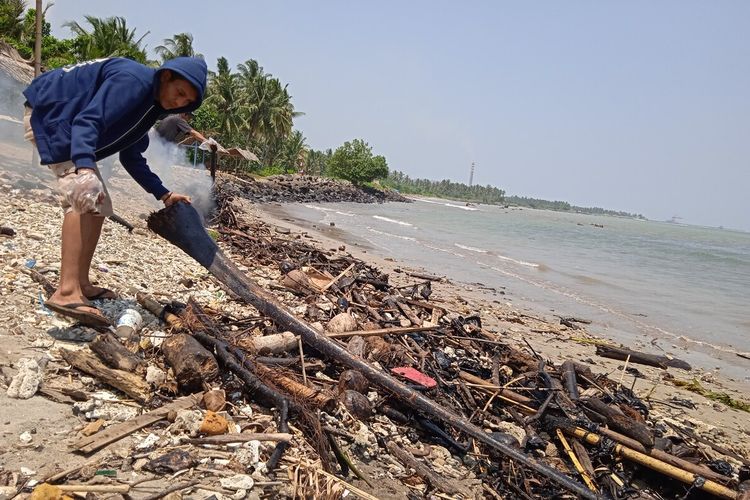 Pedagang di Pantai Sebalang, Lampung, membersihkan bibir pantai dari limbah yang mirip aspal dan oli, Jumat (10/9/2021).