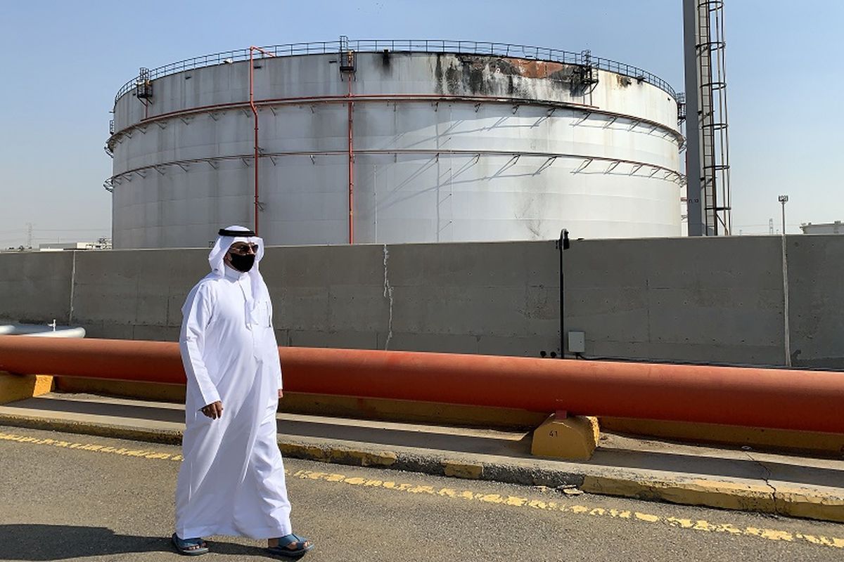 Seorang pria bermasker tampak sedang berjalan melewati tangki minyak yang rusak di fasilitas kilang minyak Saudi Aramco di kota Jeddah, Laut Merah, Arab Saudi pada 24 November 2020. 