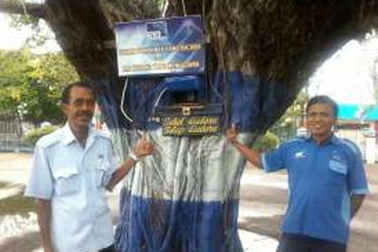 :Dua orang karyawan RRI Kupang, Nusa Tenggara Timur (NTT) sedang berdiri di depan pohon beringin yang menjadi tempat ditaruhnya radio dan tulisan bukan pohon yang bicara tapi RRI Kupang yang mengudara