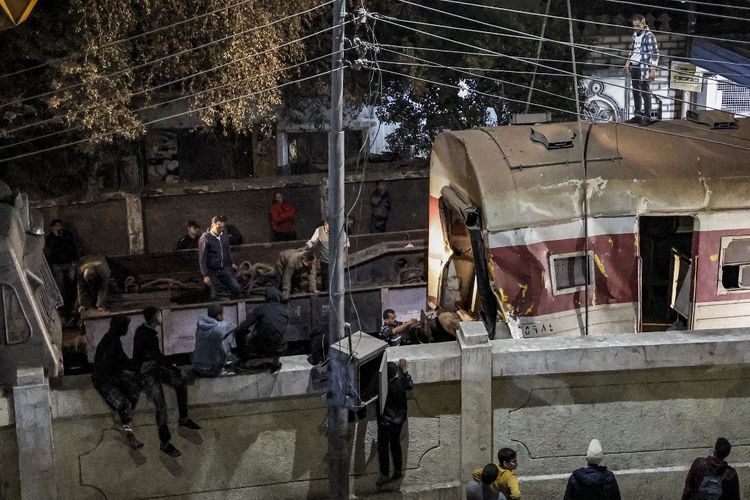 Orang-orang berkumpul di dekat tembok yang memagari jalur kereta api saat derek dikerahkan untuk mengangkat kereta yang tergelincir di lokasi kecelakaan kereta api di kota Qalyub, provinsi Qalyub, di wilayah delta Nil Mesir di utara ibu kota Kairo pada Selasa (7/3/2023).