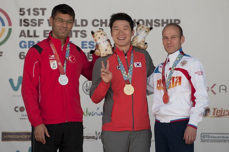 Atlet menembak Korea Selatan Jin Jong-oh berpose dengan medali emas yang diraihnya dalam Kejuaraan Dunia ISSF ke-51 di Las Gabias, dekat Granada, pada 11 September 2014. Di sebelahnya adalah Yusuf Dikec (Turki, kiri), dan Vladimir Gontcharov (Rusia, kanan). Jin meraih emas di nomor 10 meter air pistol.