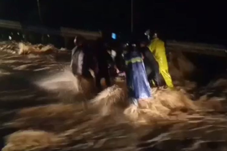 Warga saat mencoba berjalan di tengah derasnya banjir di jalan raya kawasan Jelun, Kecamatan Licin