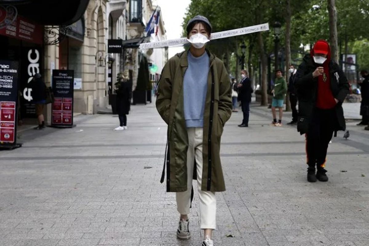 Seorang perempuan melintas di sebuah jalan di Paris dengan topi bertanda khusus. Tanda tersebut memiliki tulisan untuk meminta orang menjaga jarak demi mencegah penularan Covid-19.0