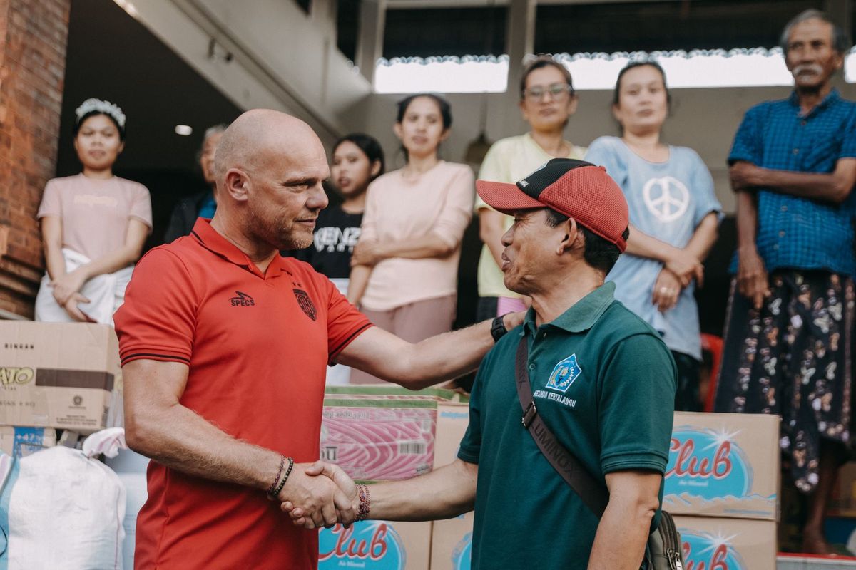 Pelatih Bali United Johnny Jansen bersalaman dengan Kepala Desa Kesiman, Kertalangu, I Made Suena saat aksi sosial memberikan bantuan kepada korban banjir di Posko Pengungsian Banjar Tohpati, Desa Kesiman Kertalangu, Denpasar Timur, Kamis (11/9/2025) sore.