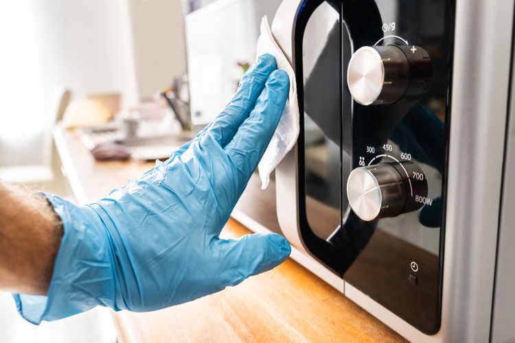 Ilustrasi membersihkan microwave dengan tisu basah antibakteri.