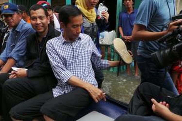 Gubernur DKI Jakarta Joko Widodo membuang air yang masuk sepatunya saat duduk di perahu ketika mengunjungi lokasi banjir dan rumah pompa Pluit, Jakarta Utara, Minggu (19/1/2014).