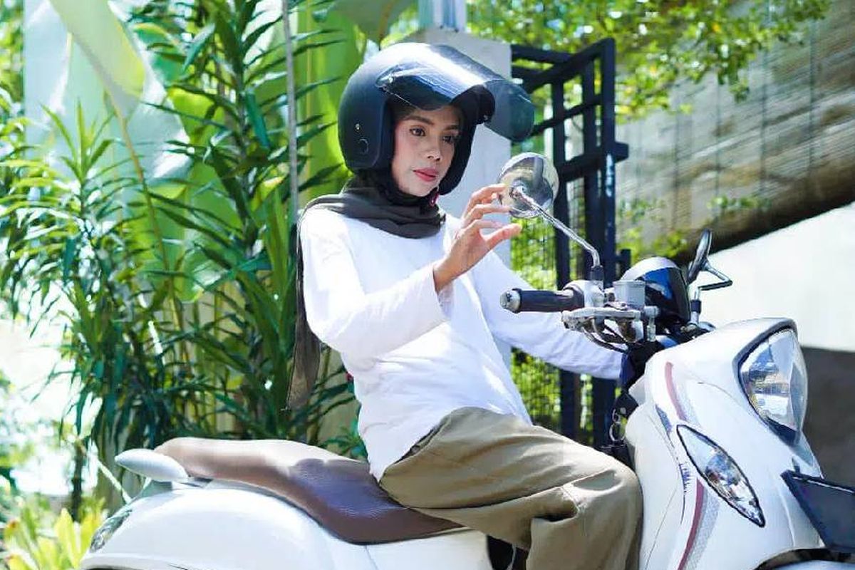 Ilustrasi wanita berkerudung mengendarai motor.