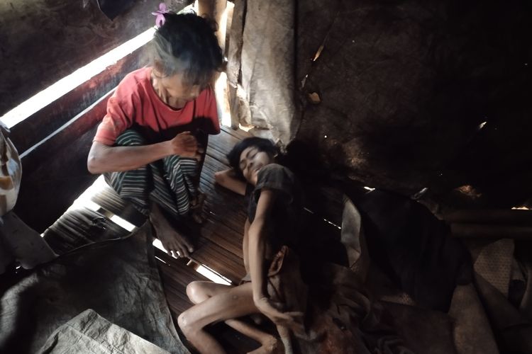 Regina Roghong (66) duduk disamping anaknya yang derita lumpuh layu di kamar tidurnya di Kampung Mesi, Dusun Mesi, Desa Ranakolong, Kecamatan Kota Komba, Kabupaten Manggarai Timur, NTT, Sabtu, (17/11/2023). (KOMPAS.com/MARKUS MAKUR)