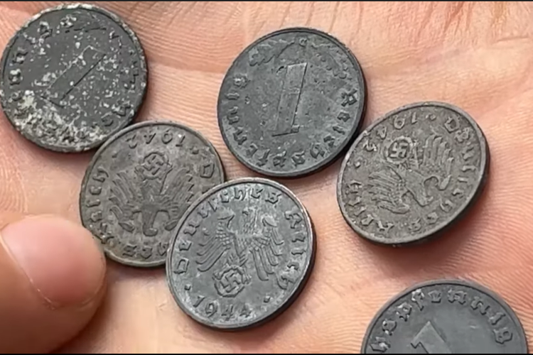 Tangkap layar enam koin pfennig Reichsbank yang ditandai dengan Swastika ditemukan di istana Polandia di desa Minkowskie, saat tim pemburu harta karun nazi membersihkan tanah dari salah satu dari tiga lokasi yang sedang diselidiki.
