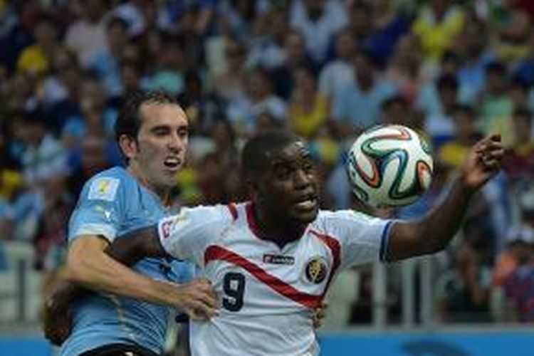 Striker Kosta Rika, Joel Campbell (kanan), berebut bola dengan bek Uruguay, Diego Godin, pada laga perdana penyisihan Grup D Piala Dunia 2014, Sabtu (14/6/2014).